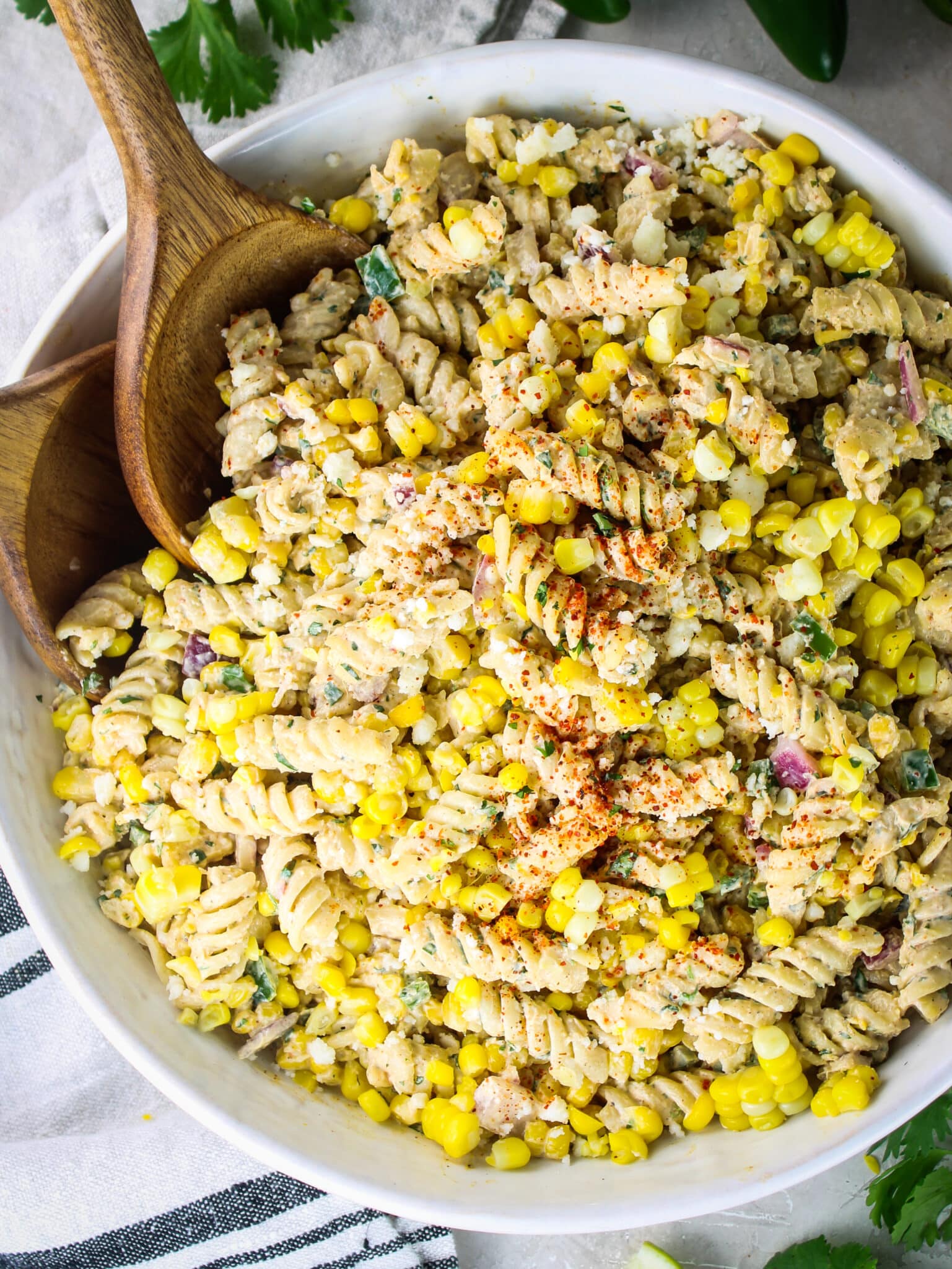 Street corn pasta salad in a white bowl with two spoons, styled next to a striped linen napkin