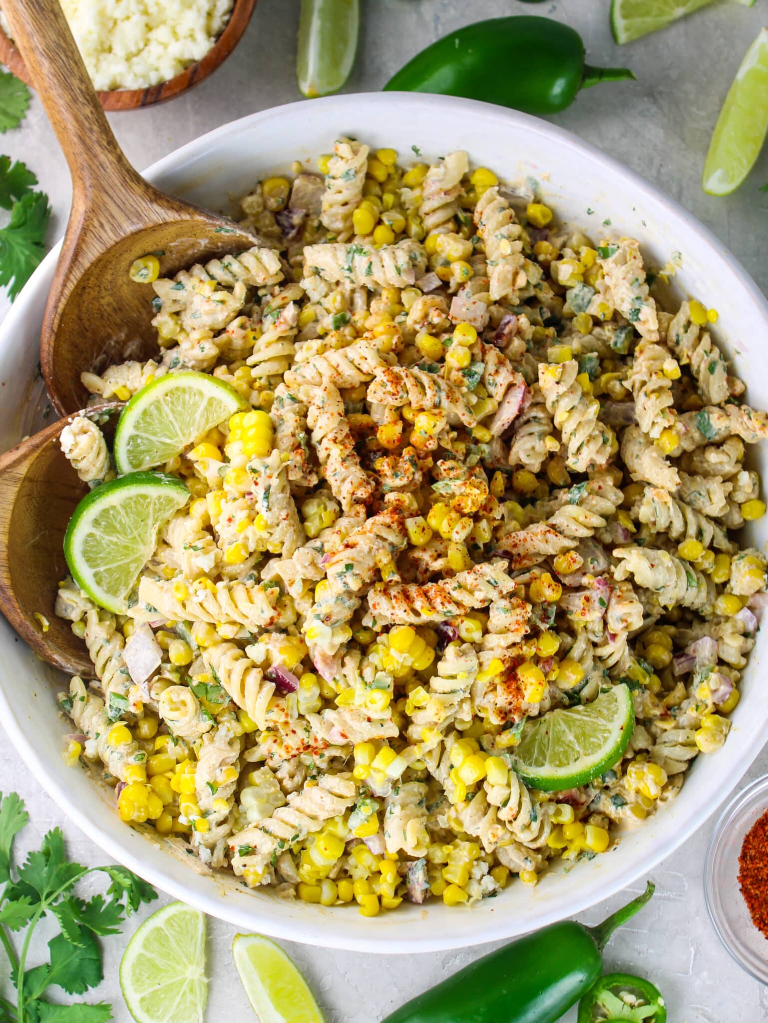 Mexican street corn pasta salad in a white bowl with fresh lime wedges, jalapeño, and cotija cheese on the side