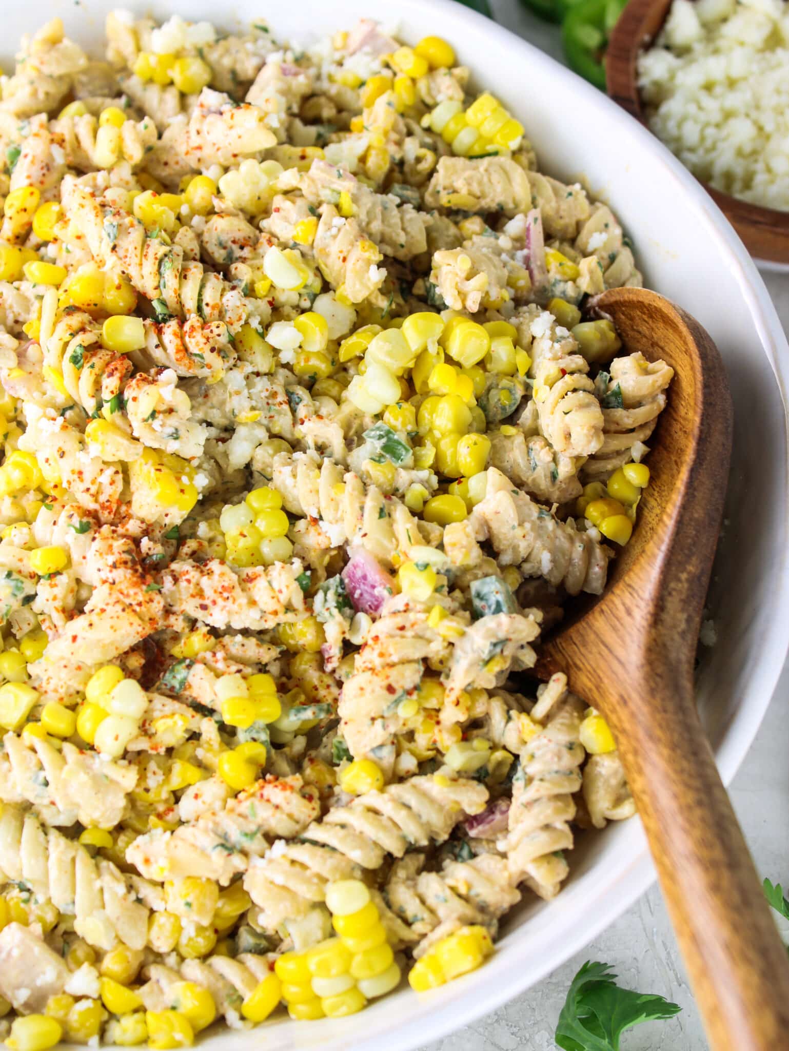 Detail shot of rotini pasta salad with corn, cotija, and a wooden spoon resting in the bowl